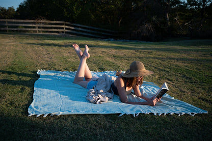 An image of a woman reading outside on the palmetto green blanket.