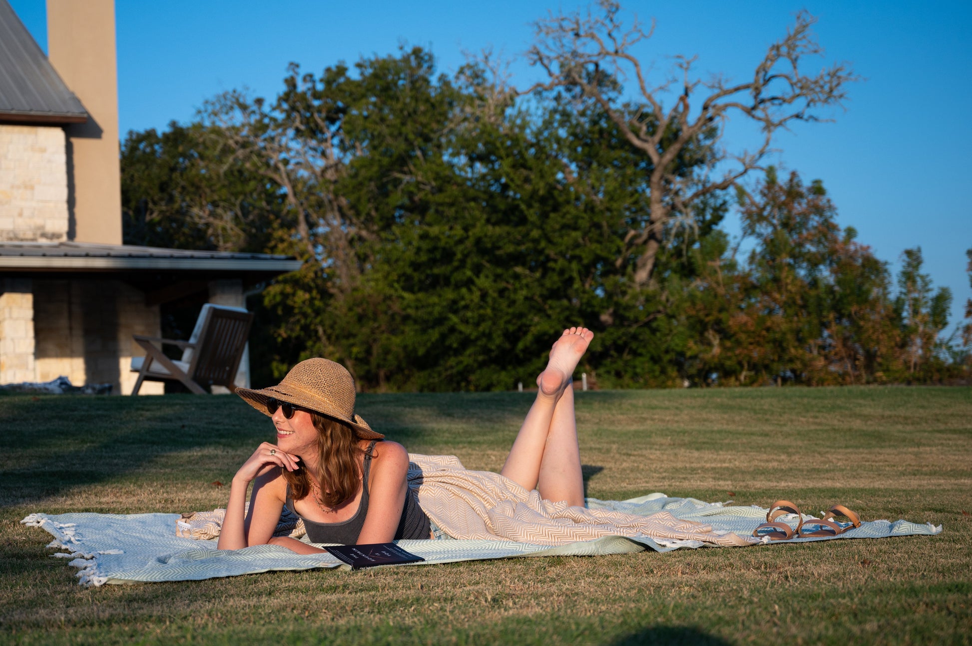 A woman posing while using the herringbone throw blanket as a picnic blanket with both the palmetto green and desert stone throw blankets visible.