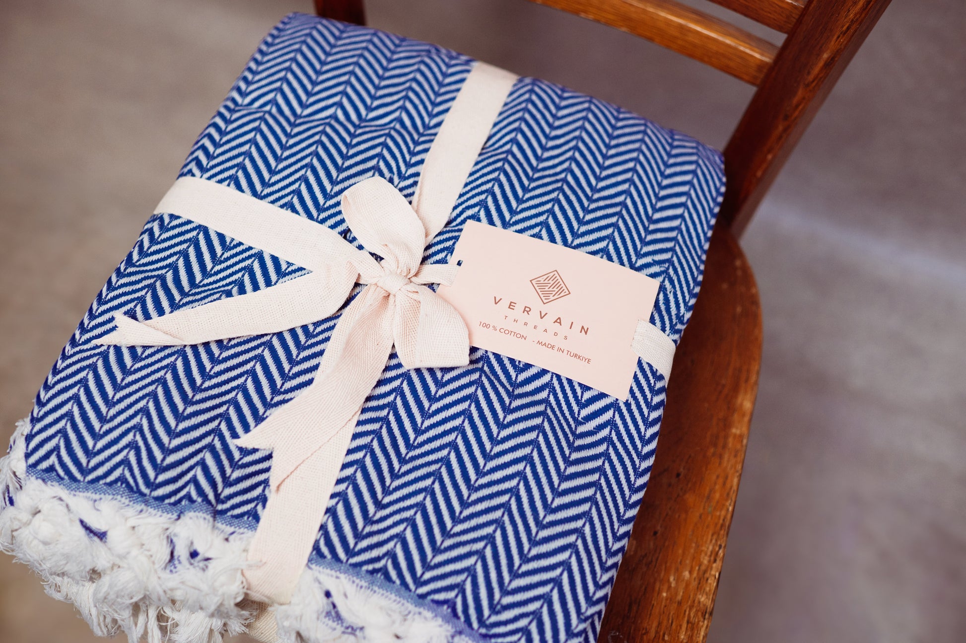 An image of the blue herringbone throw blanket tied up and sitting on a chair.