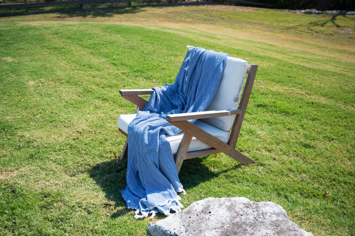 Another perspective of the blanket draped over a chair with the sunlight illuminating the deep ocean blue color.